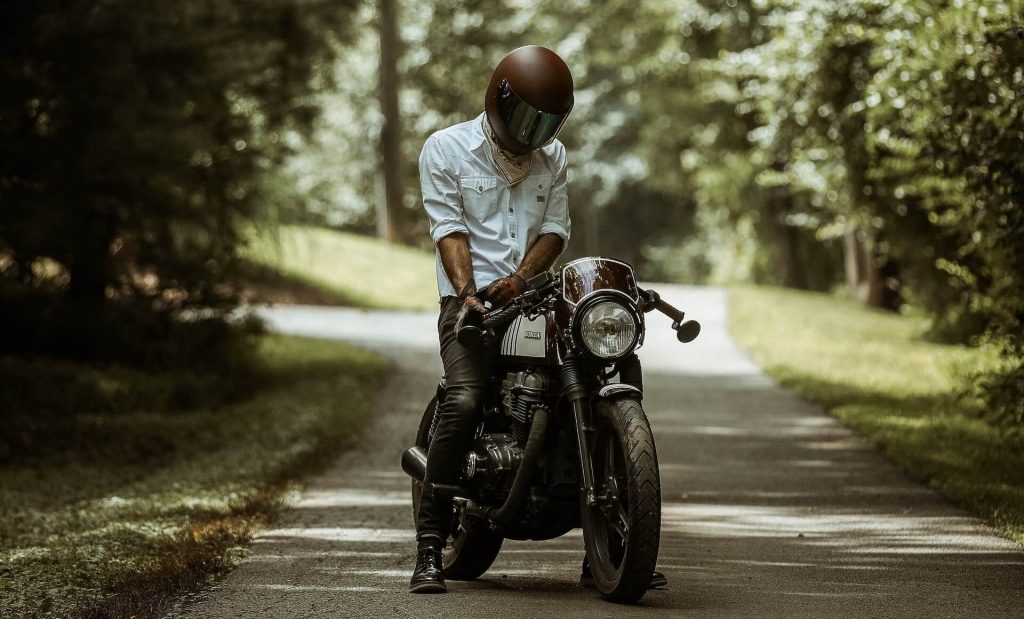 A man confidently riding a motorcycle on a deserted road surrounded by lush trees.
