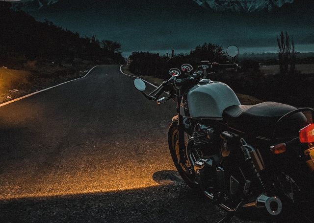 A motorcycle with its headlights illuminated, cruising down a dimly lit road.